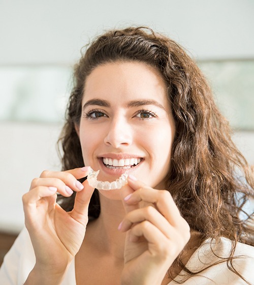 young woman smiling while holding clear aligners 