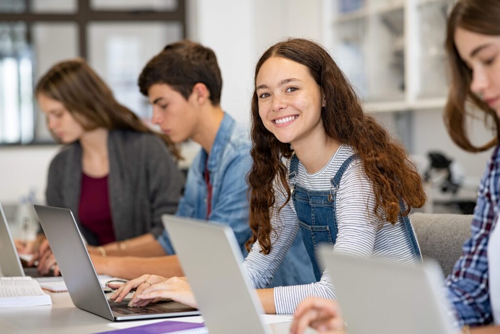 Teen smiling while working on laptop at school